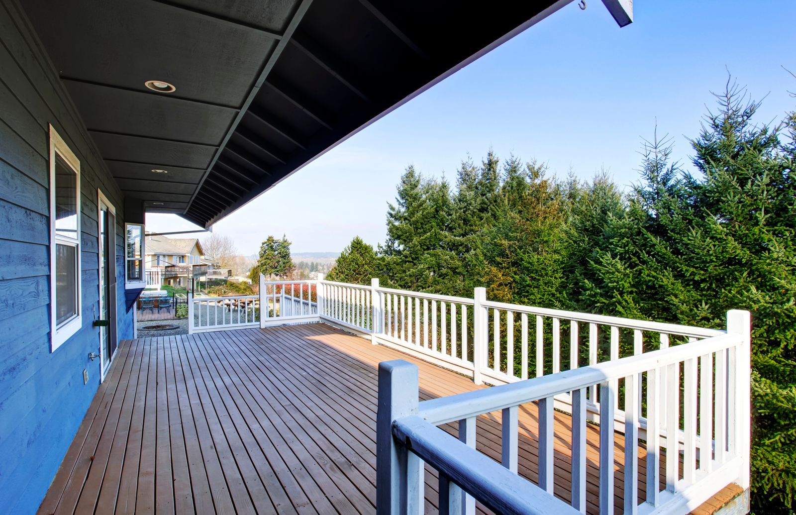 A finished deck with white railings beside a blue house